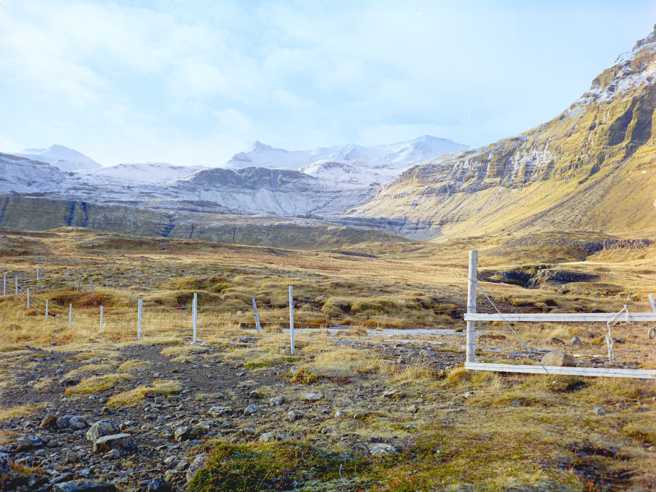 an old, wood and cable fence stretching across a lush green valley below dramatic, snowcapped peaks