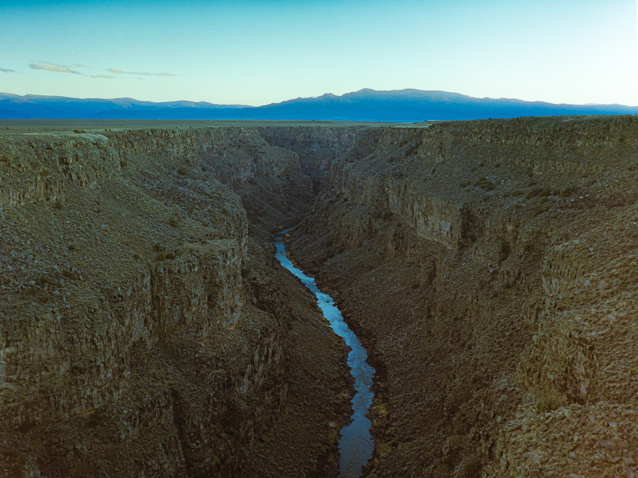 A view from above the rio grande river gorge with a warm, setting sun creating a warm glow along the mountains that stretch across the horizon