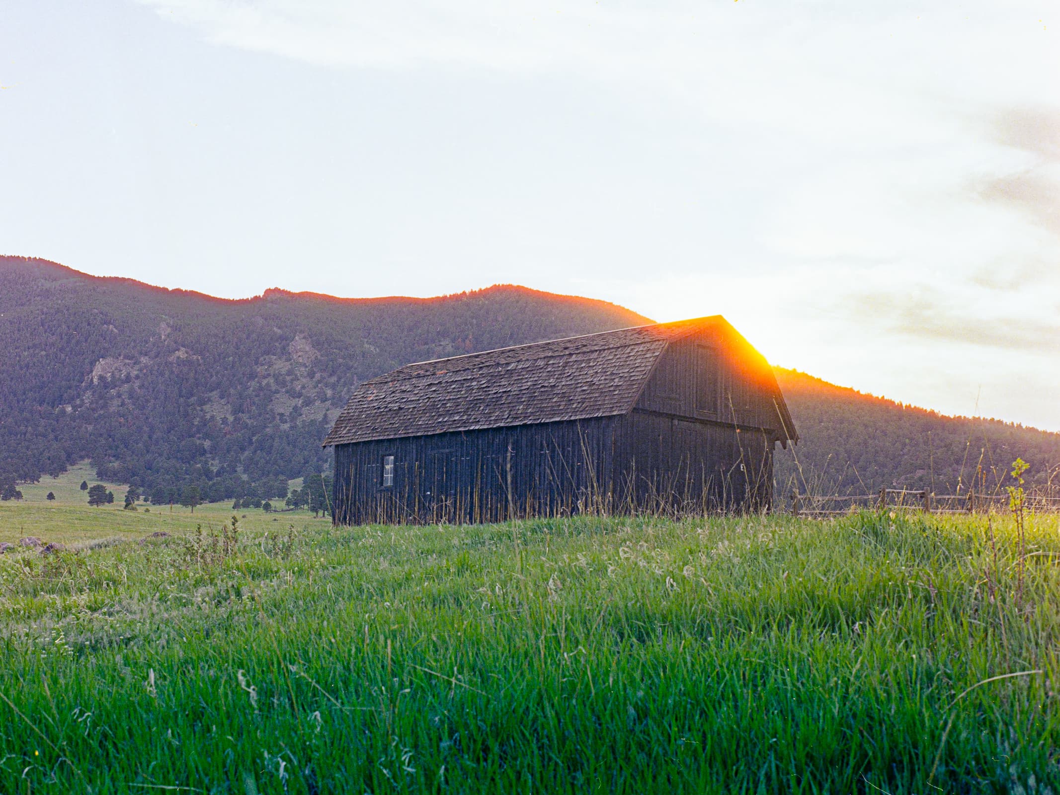 An old barn in a meadow below a large forested hill