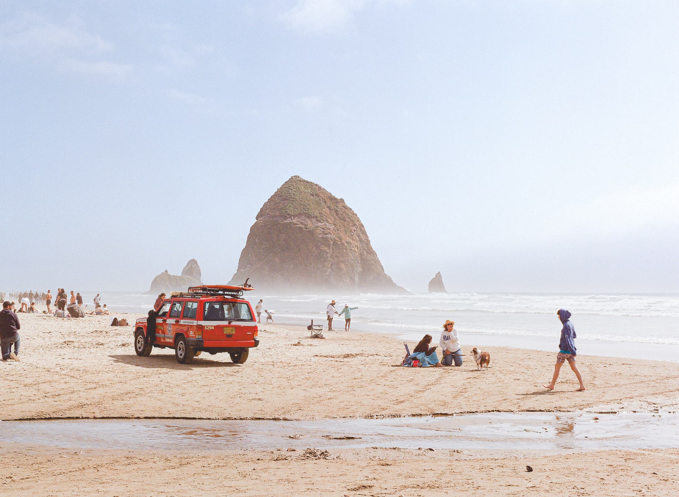 many people gathered on a busy beach near a large sea stack on Canon Beach on the Oregon Coast